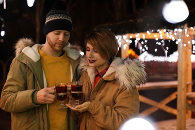 Photo of Young couple with cups of mulled wine at winter fair