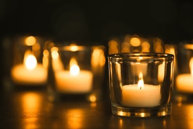 Photo of Burning candles on table in darkness. Funeral symbol