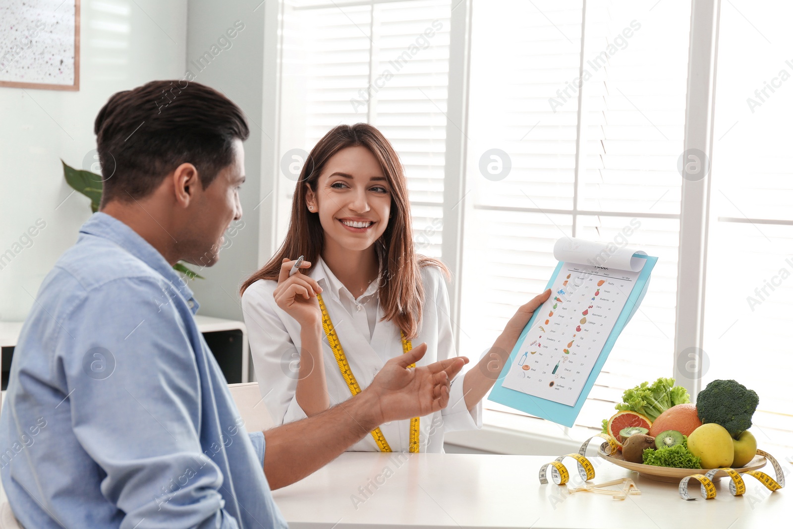 Photo of Young nutritionist consulting patient at table in clinic