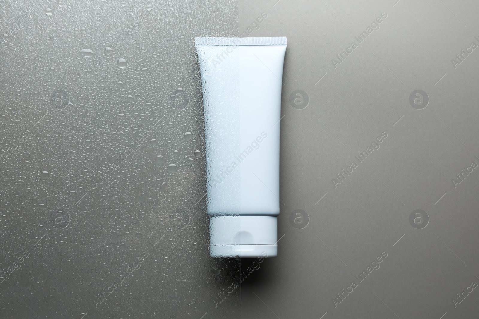 Photo of Tube with moisturizing cream on wet grey surface, top view