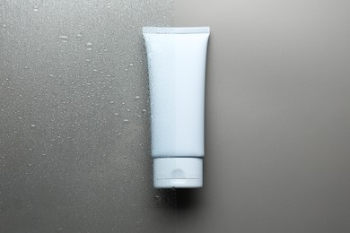 Photo of Tube with moisturizing cream on wet grey surface, top view