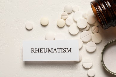 Card with word Rheumatism and pills on white textured background, flat lay