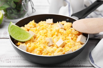 Frying pan with delicious scrambled eggs, tofu and lime on white wooden table