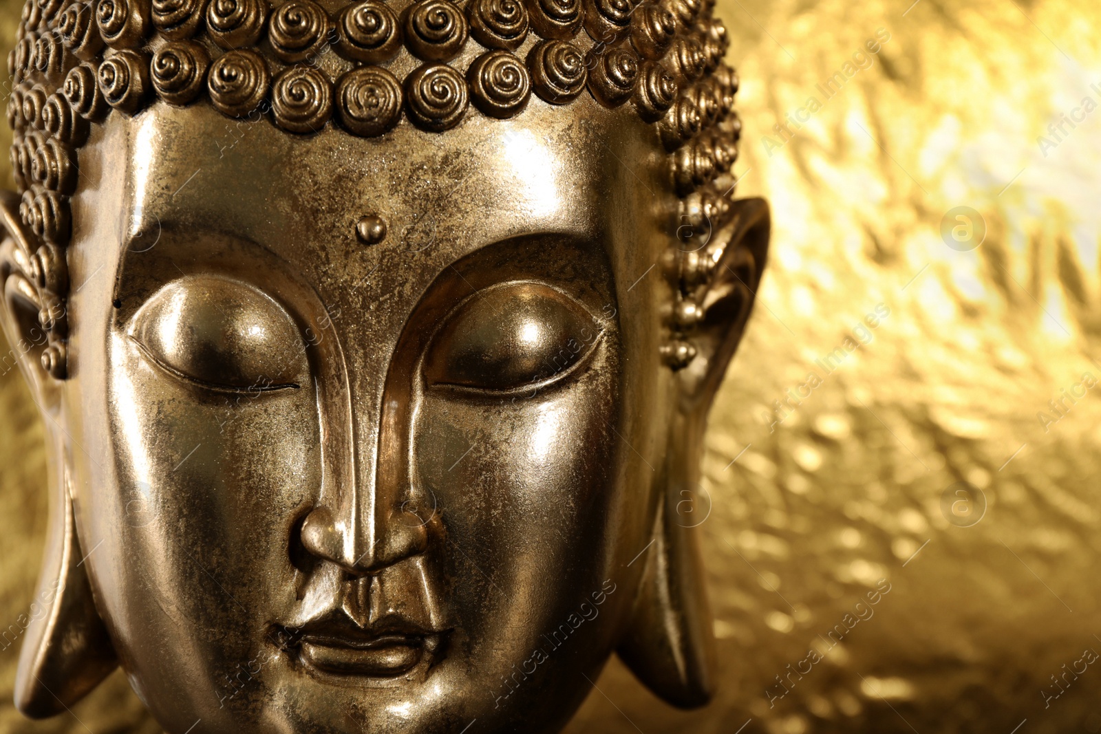 Photo of Buddha statue on golden background, closeup. Space for text