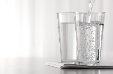 Photo of Pouring water into glass at table against blurred background. Space for text