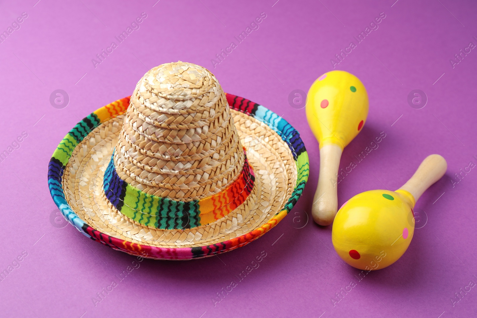 Photo of Mexican sombrero hat and maracas on purple background