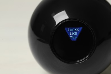 Photo of Magic eight ball with prediction Looks Like Yes on light background, closeup