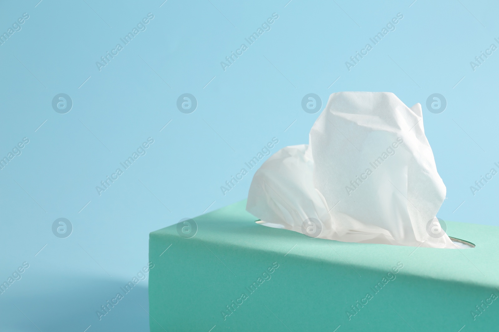 Photo of Box of paper tissues on light blue background, closeup. Space for text