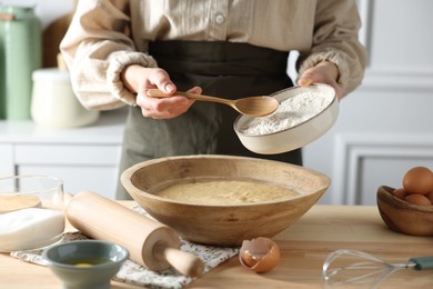 Making dough. Woman adding flour into bowl at wooden table in kitchen, closeup