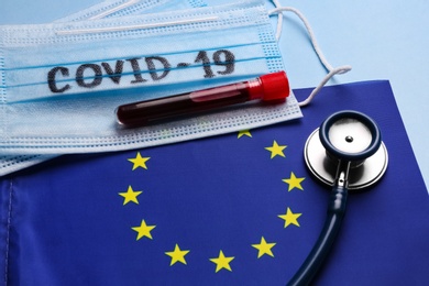 Photo of European Union flag, protective masks and test tube with blood sample on light blue background. Coronavirus outbreak
