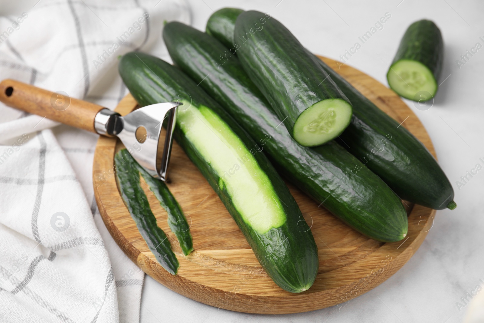 Photo of Fresh cucumbers and peeler on white table, closeup