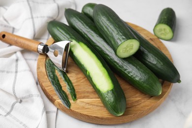 Photo of Fresh cucumbers and peeler on white table, closeup