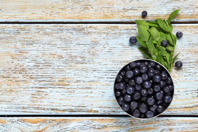 Ripe bilberries in bowl and sprigs with leaves on wooden rustic table, flat lay. Space for text