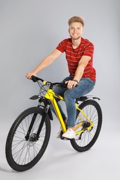 Handsome young man riding bicycle on grey background