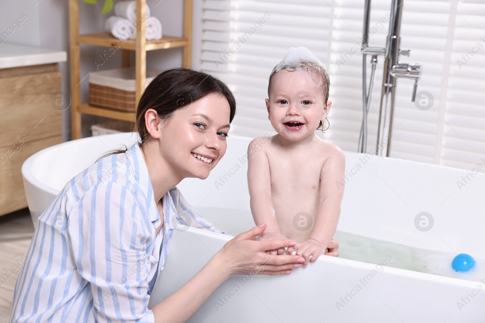 Photo of Mother bathing her cute little baby in tub at home