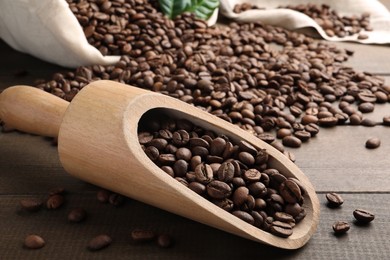 Photo of Scoop with roasted coffee beans on wooden table, closeup