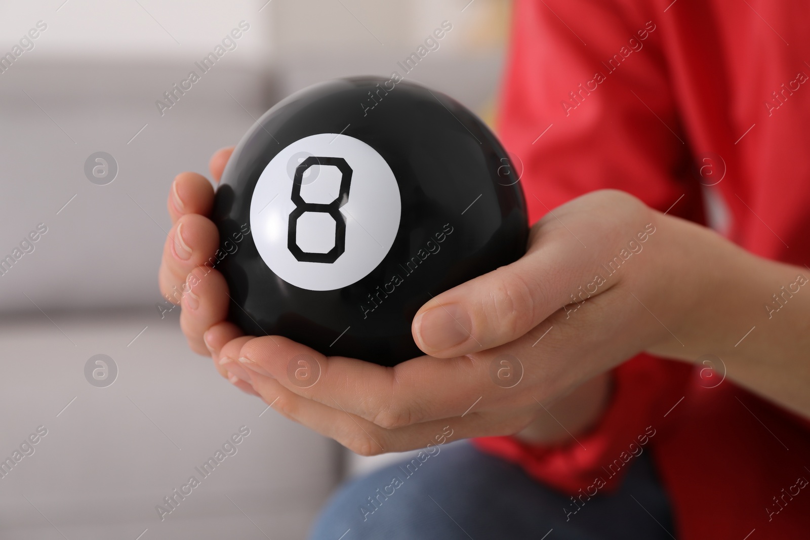 Photo of Woman holding magic eight ball indoors, closeup