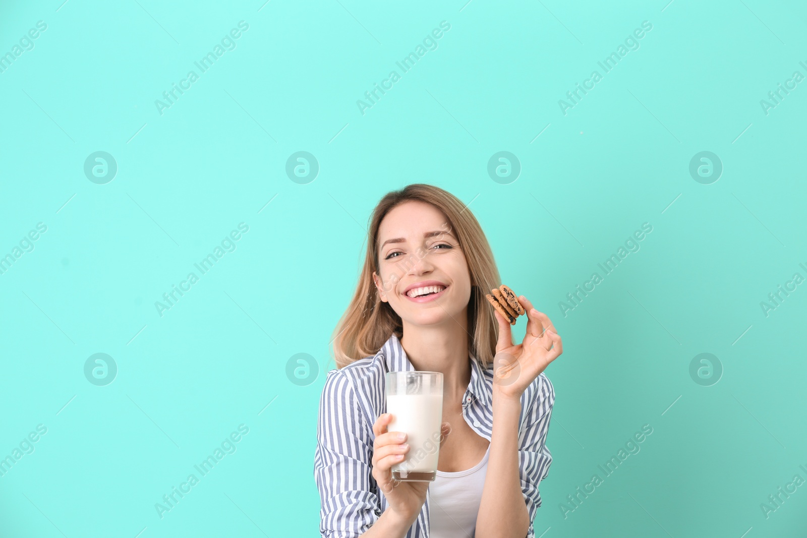 Photo of Beautiful young woman drinking milk with cookies on color background