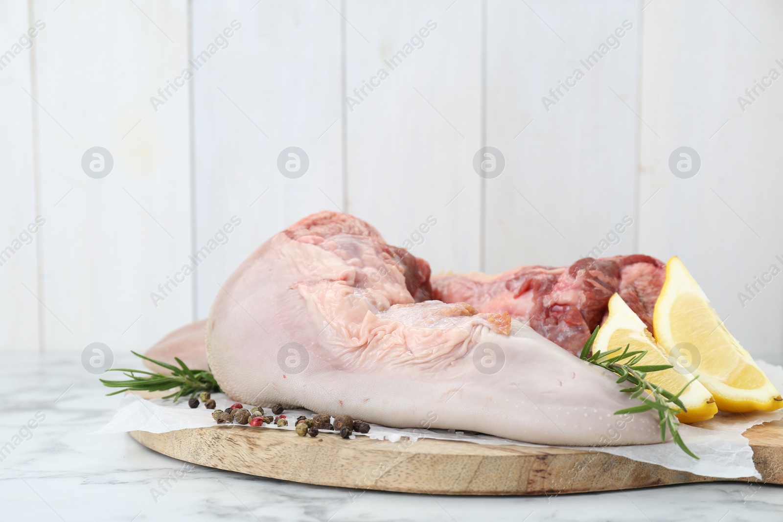 Photo of Raw beef tongues, peppercorns, salt, rosemary and lemon on white marble table, closeup