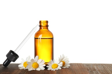 Bottle of herbal essential oil, pipette and chamomile flowers on wooden table, white background