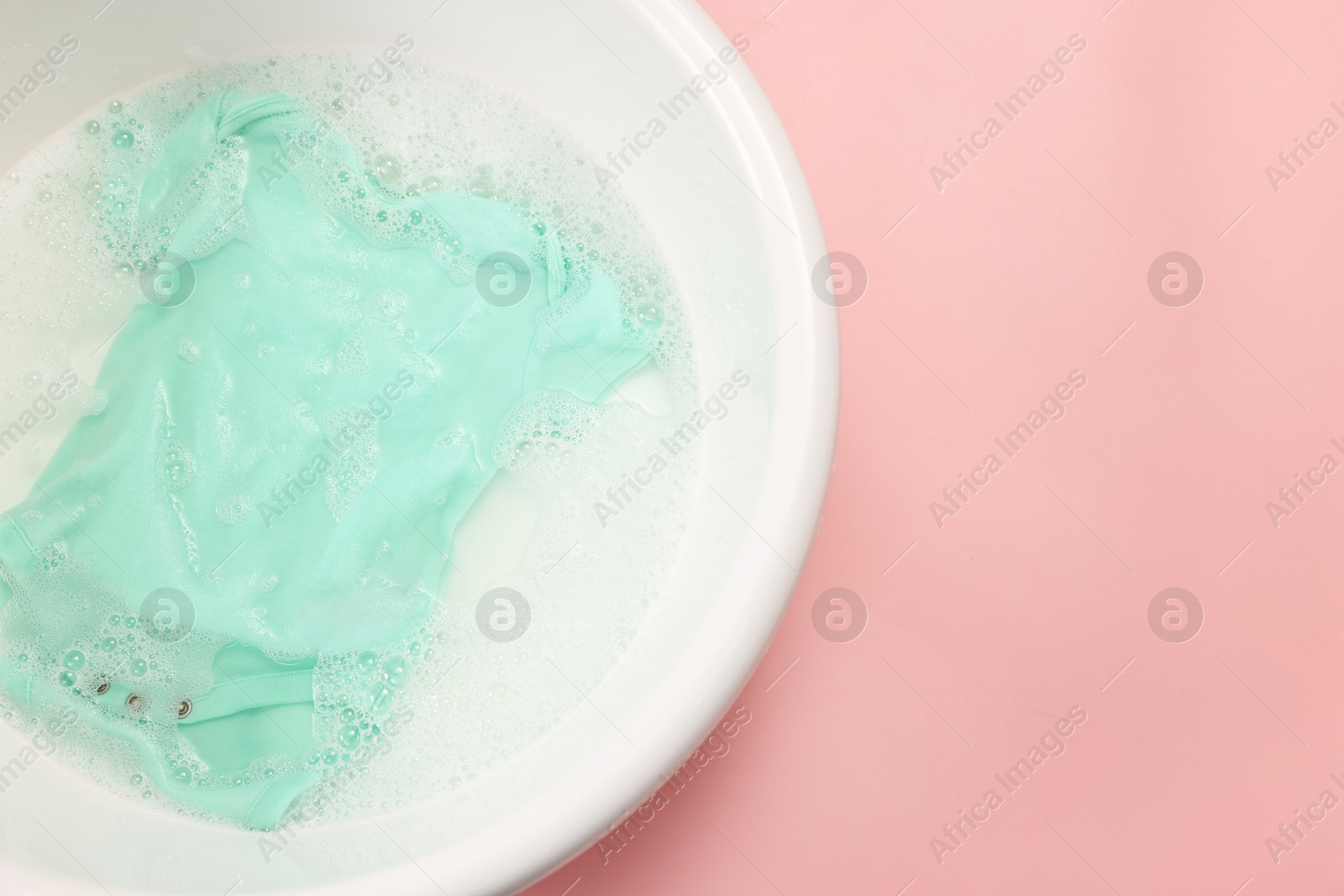 Photo of Baby clothes in washing basin on pink background, top view. Space for text