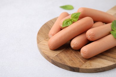 Delicious boiled sausages and basil on light gray table, closeup. Space for text