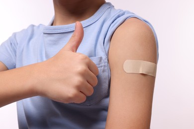 Photo of Boy with sticking plaster on arm after vaccination showing thumbs up against white background, closeup
