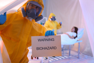 Photo of Paramedic holding sign with words WARNING BIOHAZARD in quarantine ward. Virus awareness