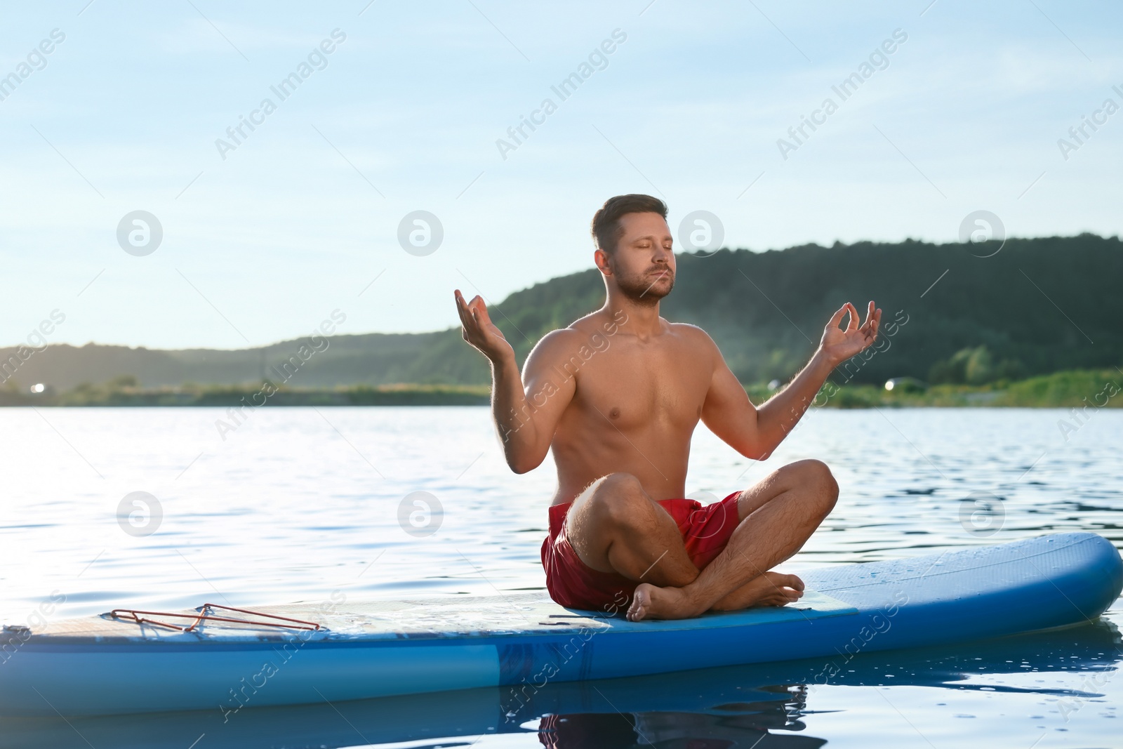 Photo of Man meditating on light blue SUP board on river at sunset