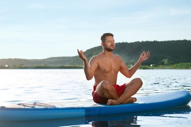 Man meditating on light blue SUP board on river at sunset
