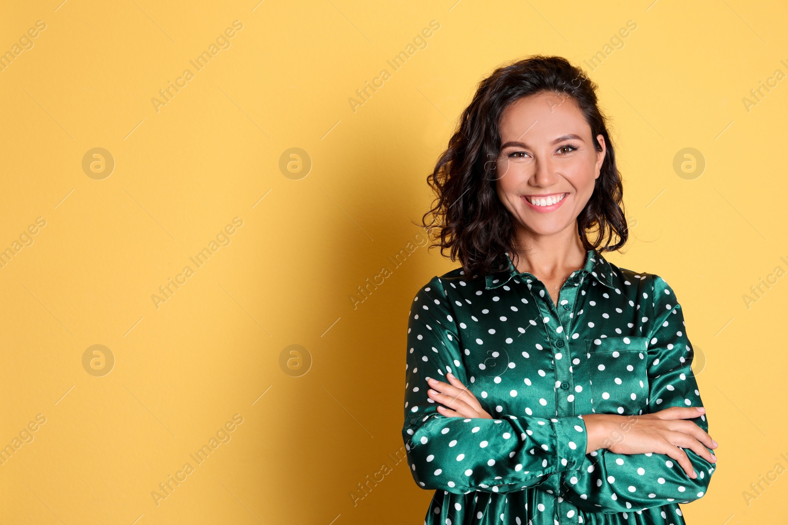 Photo of Happy young woman with crossed hands on yellow background. Space for text