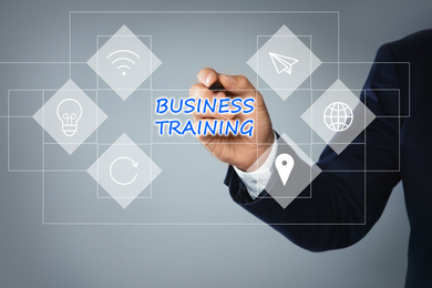 Image of Man pointing at virtual screen with inscription BUSINESS TRAINING on light background, closeup 