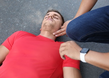 Photo of Passerby checking pulse of unconscious young man outdoors