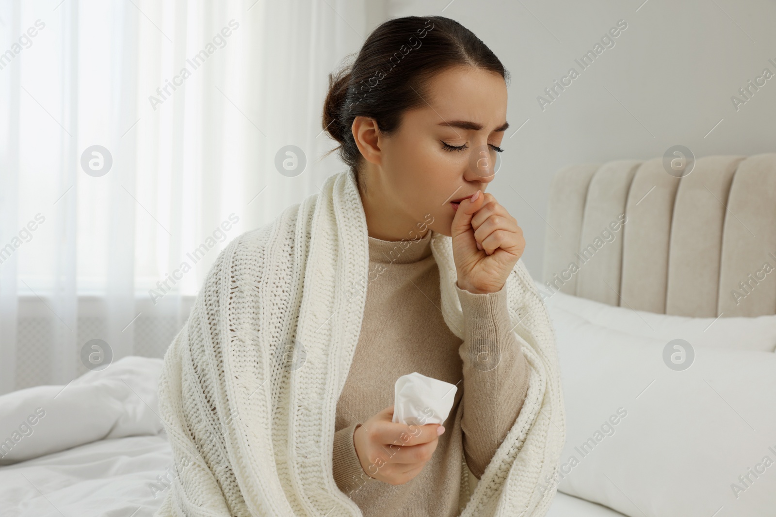 Photo of Sick young woman with tissue wrapped in knitted plaid at home