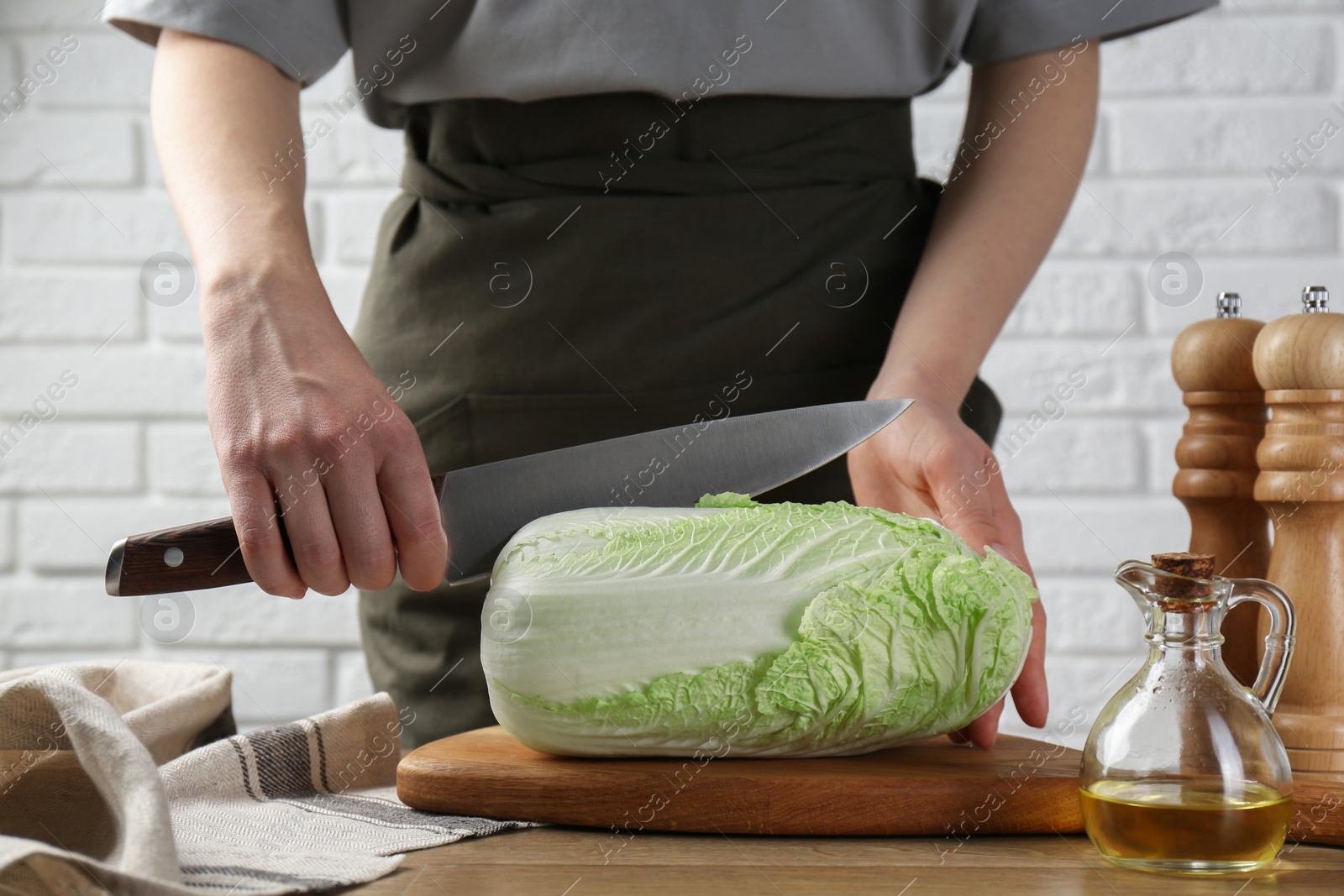 Photo of Woman cutting fresh Chinese cabbage at wooden table indoors, closeup