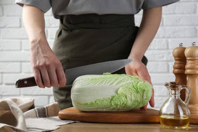 Photo of Woman cutting fresh Chinese cabbage at wooden table indoors, closeup