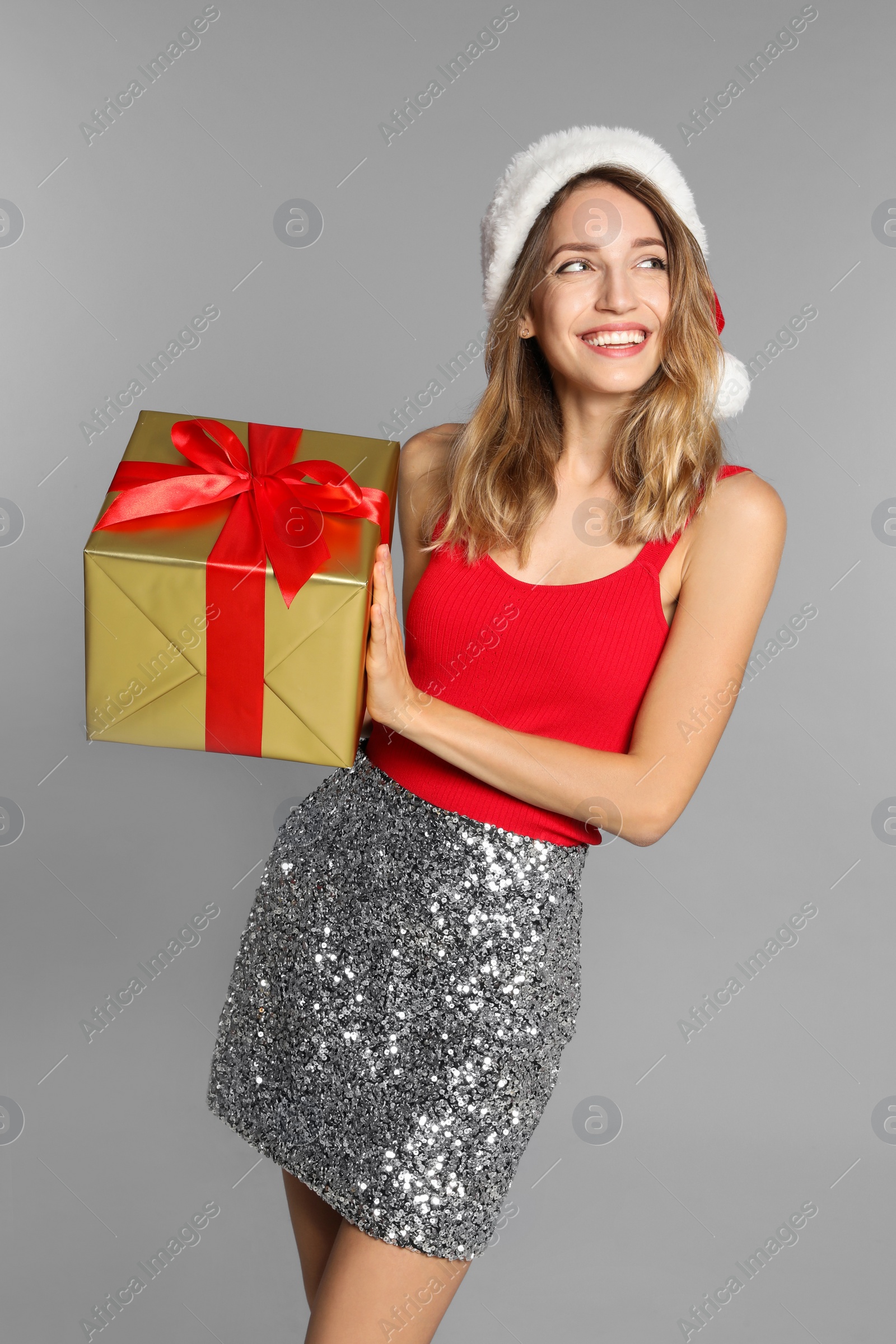 Photo of Happy young woman in Santa hat with gift box on light grey background. Christmas celebration