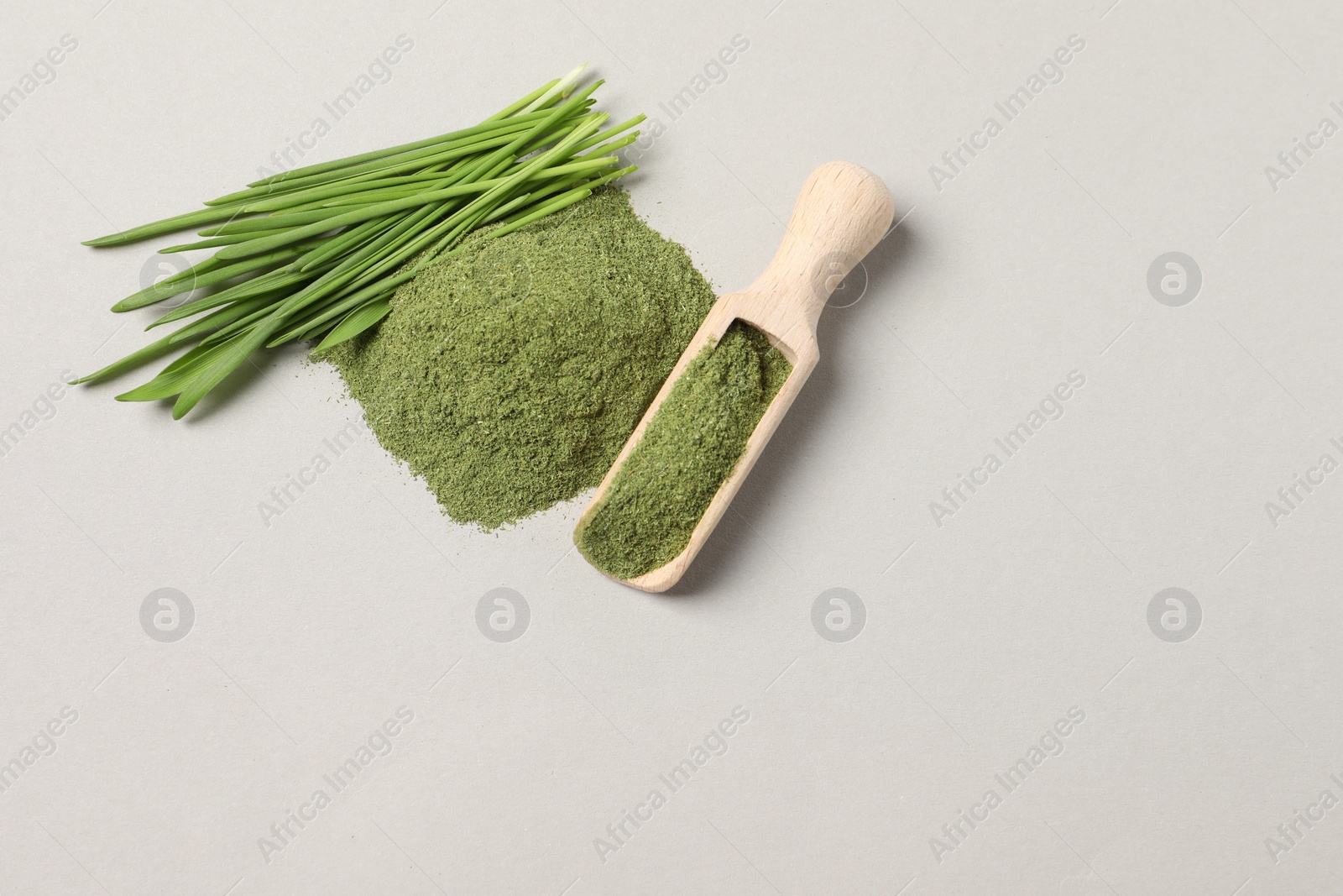 Photo of Pile of wheat grass powder, scoop and fresh sprouts on light grey table, flat lay. Space for text