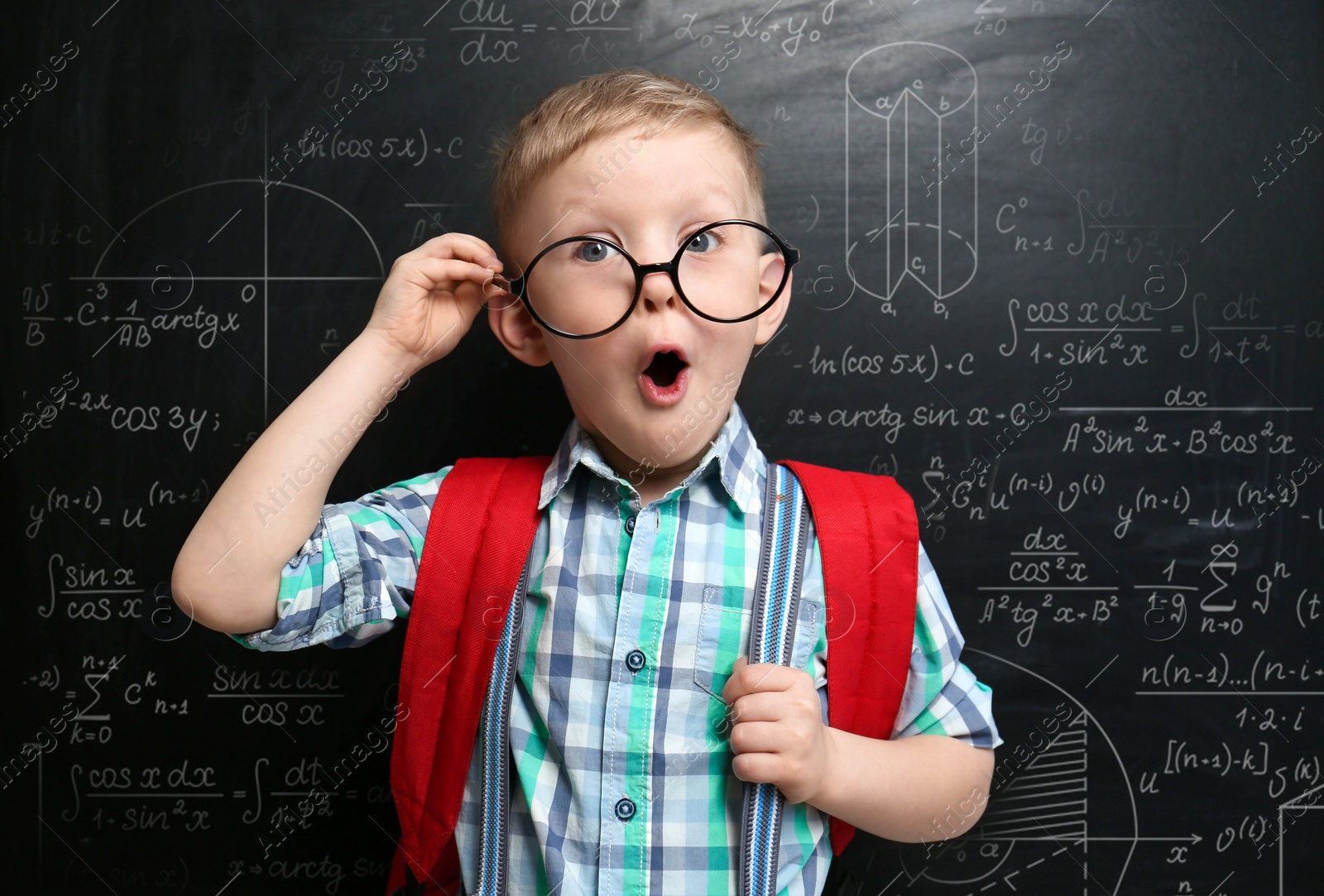 Image of Funny little child wearing glasses near chalkboard with different formulas