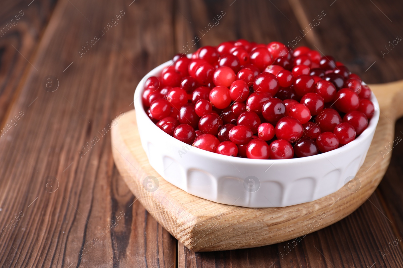 Photo of Fresh ripe cranberries in bowl on wooden table, closeup