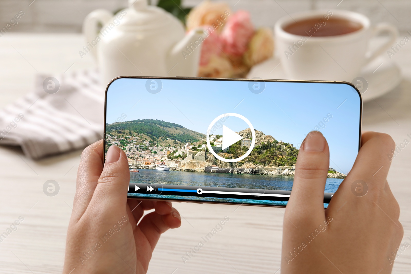 Image of Woman watching video on mobile phone at white wooden table during coffee time, closeup