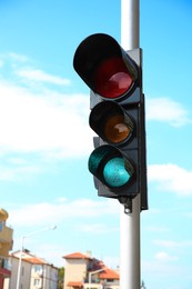 Traffic light with green sign against cloudy sky in city