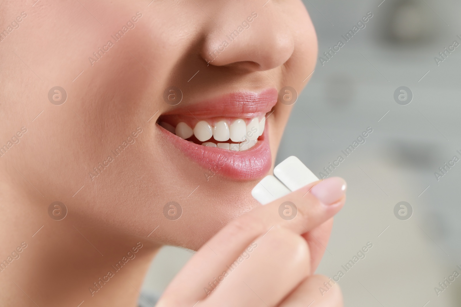 Photo of Woman putting chewing gum pieces into mouth on blurred background, closeup