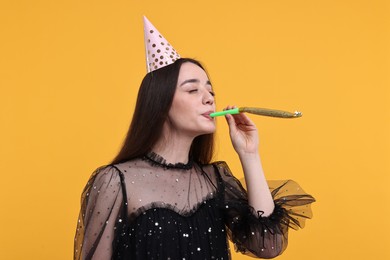 Photo of Woman in party hat with blower on orange background