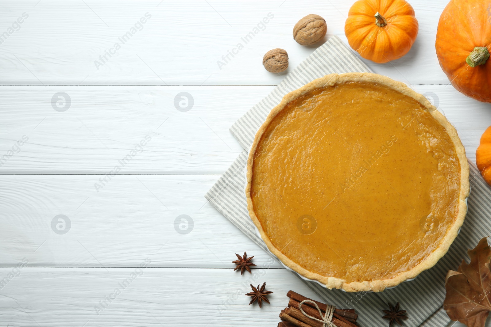 Photo of Delicious pumpkin pie and ingredients on white wooden table, flat lay. Space for text