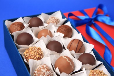 Photo of Box with delicious chocolate candies on blue background, closeup