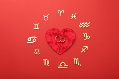 Photo of Zodiac signs, heart and wedding rings on red background, flat lay