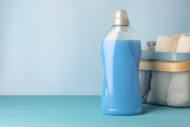 Photo of Bottle of fabric softener and towels in basket on light blue table, space for text