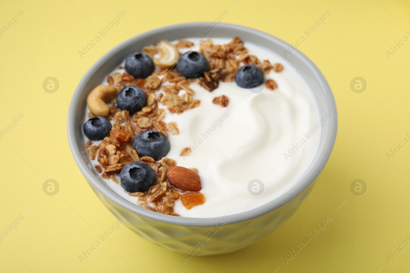 Photo of Bowl with yogurt, blueberries and granola on yellow background, closeup