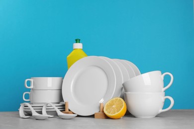Photo of Clean tableware, dish detergent and lemon on grey table against light blue background